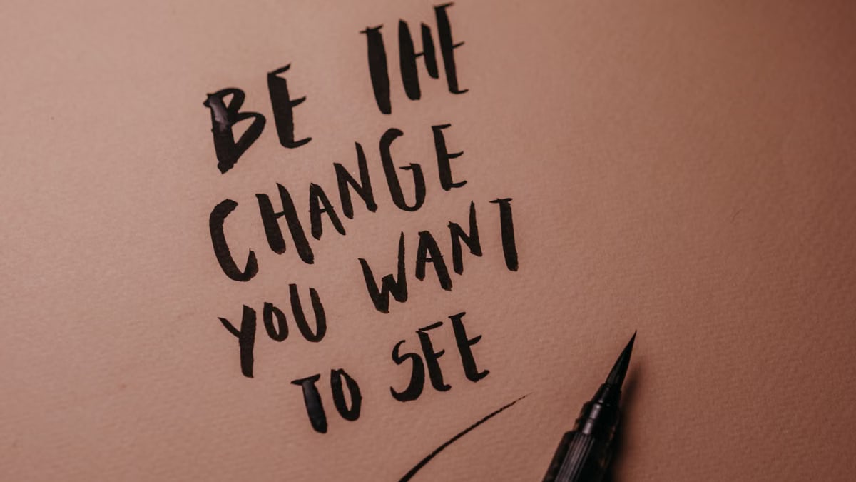 Motivational calligraphy reads 'Be the change you want to see' on a pink surface.
